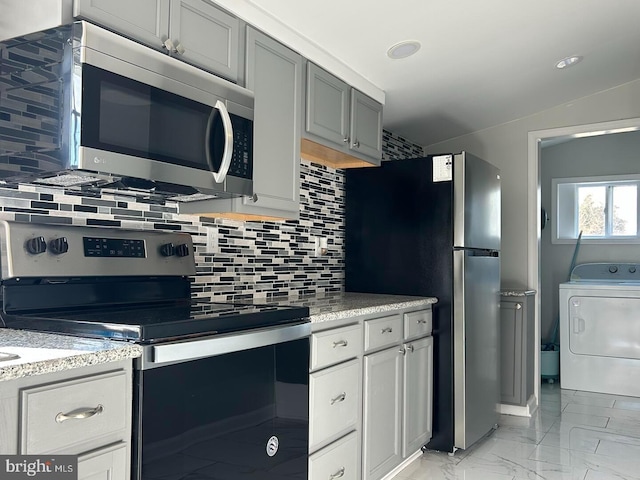 kitchen with backsplash, vaulted ceiling, gray cabinets, washer / clothes dryer, and appliances with stainless steel finishes