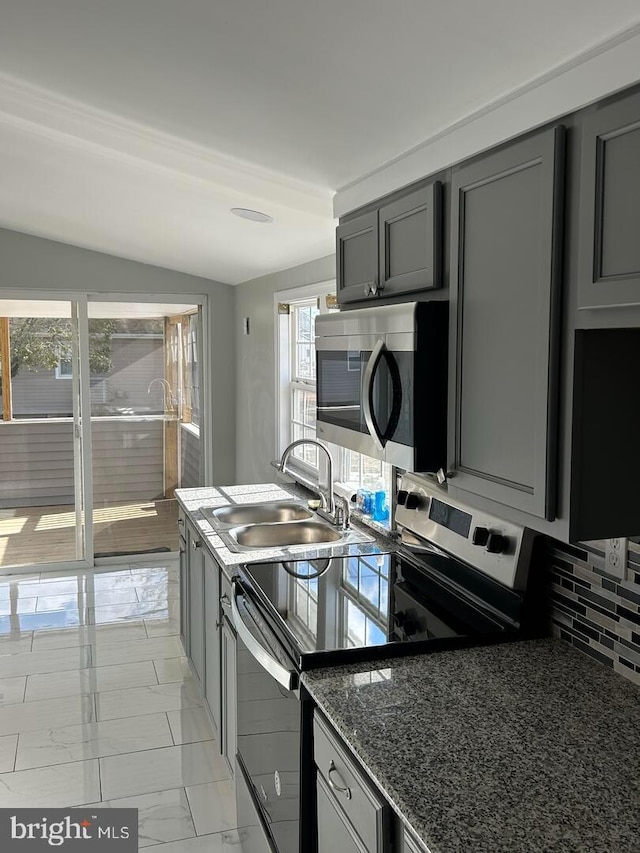 kitchen with stainless steel appliances, dark stone counters, decorative backsplash, sink, and vaulted ceiling