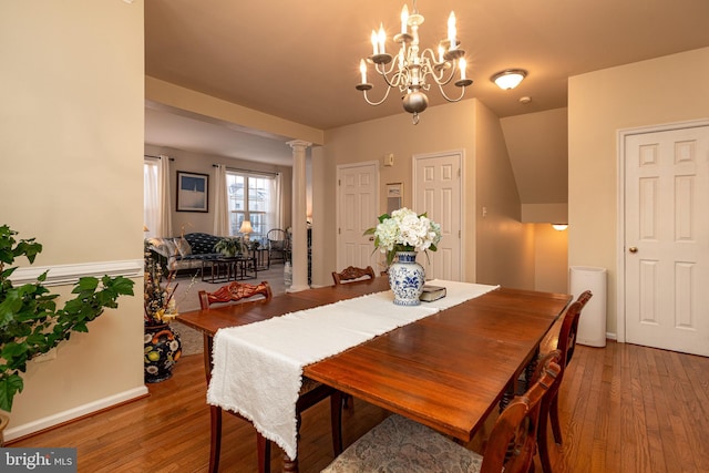 dining space with hardwood / wood-style flooring, decorative columns, and a notable chandelier