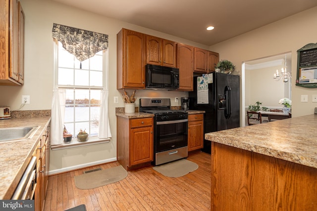 kitchen with sink, a chandelier, pendant lighting, light hardwood / wood-style floors, and black appliances