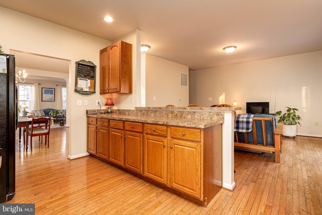 kitchen with black fridge, kitchen peninsula, an inviting chandelier, and light hardwood / wood-style flooring