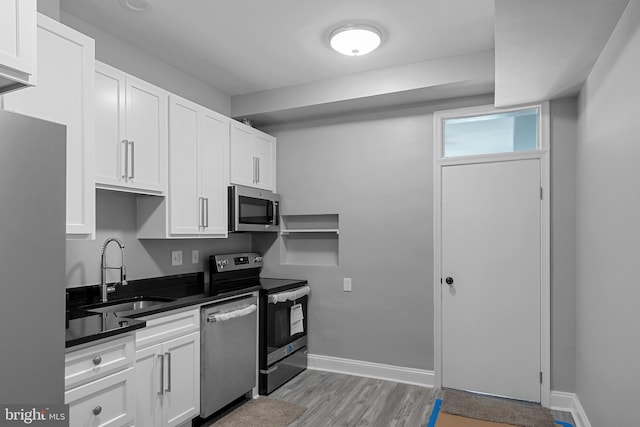 kitchen with white cabinets, appliances with stainless steel finishes, sink, and light hardwood / wood-style flooring