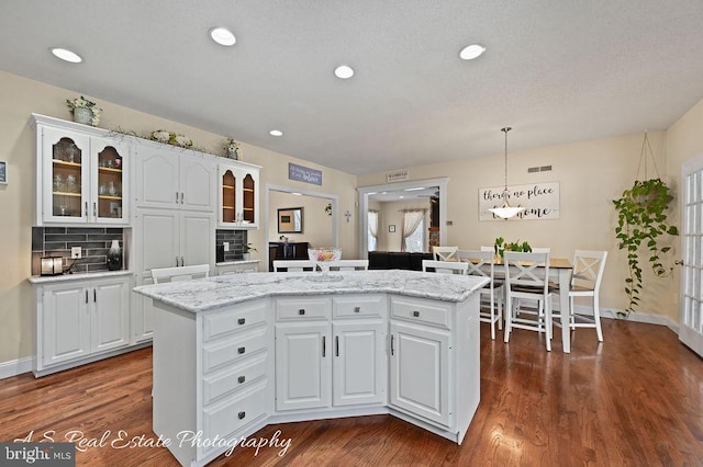 kitchen featuring white cabinets, a kitchen island, decorative light fixtures, decorative backsplash, and dark hardwood / wood-style floors