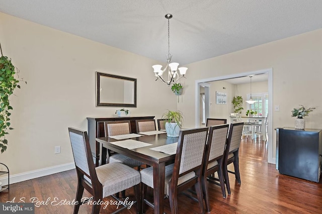 dining area featuring dark wood-type flooring, a textured ceiling, and a notable chandelier