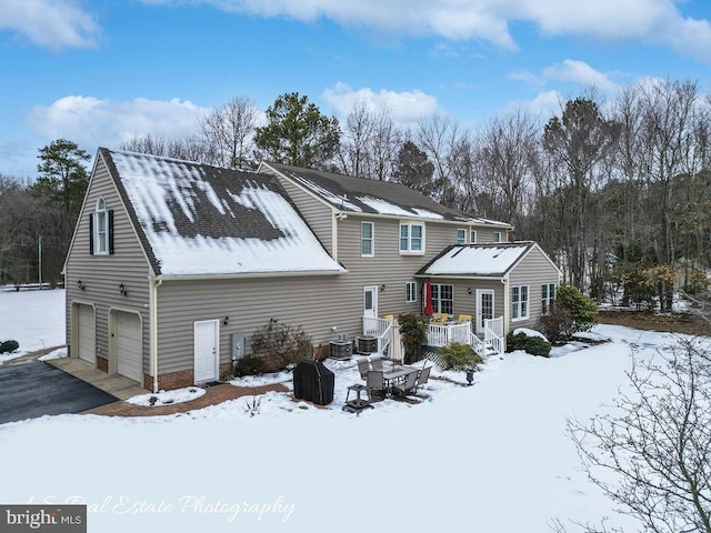 snow covered rear of property with a garage and a deck