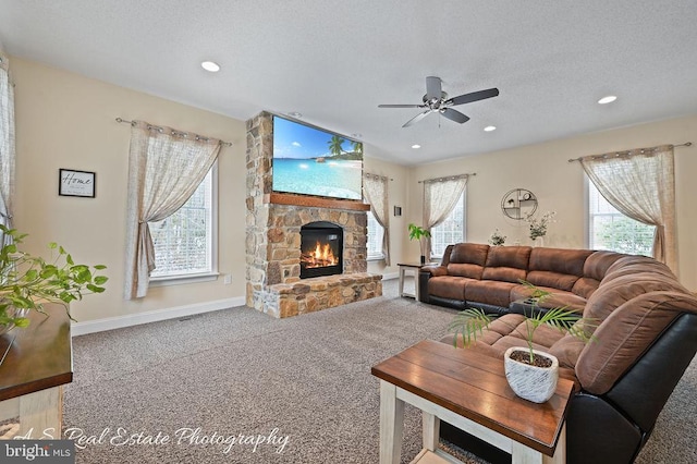 carpeted living room featuring ceiling fan, a textured ceiling, and a stone fireplace