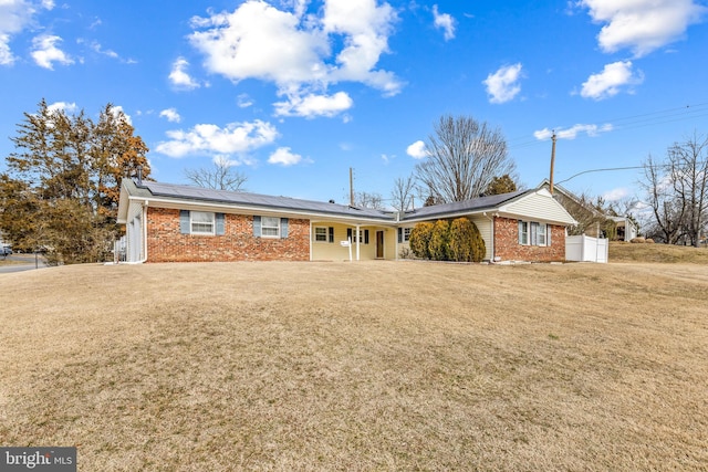 single story home with solar panels, brick siding, and a front lawn