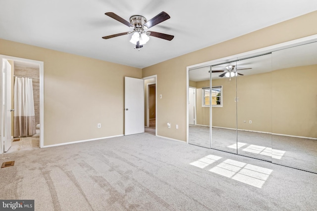 unfurnished bedroom featuring a closet, light colored carpet, ensuite bathroom, ceiling fan, and baseboards