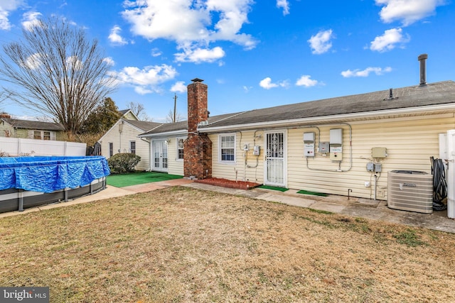 rear view of property featuring central AC unit, fence, a yard, a fenced in pool, and a chimney