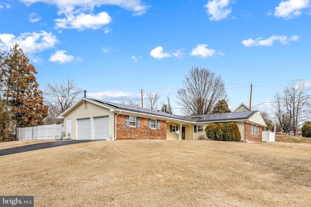 ranch-style house with aphalt driveway, an attached garage, brick siding, fence, and roof mounted solar panels