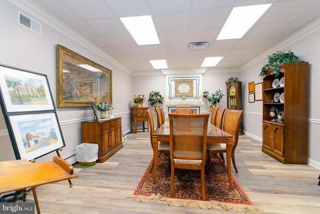 dining space with a paneled ceiling, ornamental molding, and light hardwood / wood-style flooring