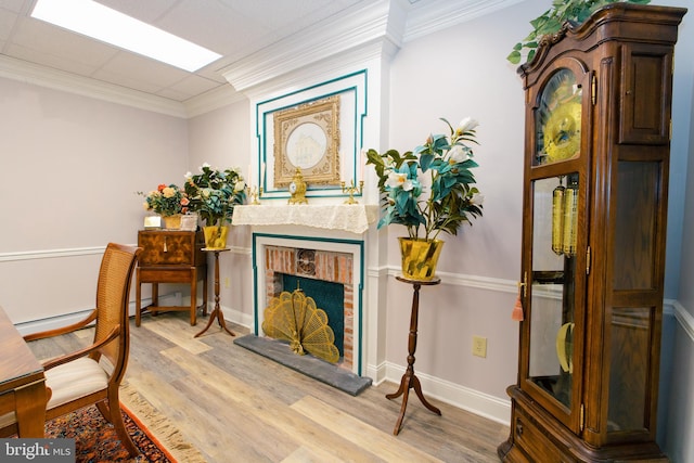 sitting room featuring a brick fireplace, ornamental molding, and light hardwood / wood-style flooring