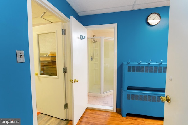 corridor with a paneled ceiling, wood-type flooring, and radiator heating unit