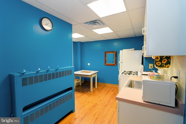 kitchen with a drop ceiling, light hardwood / wood-style flooring, radiator heating unit, and white appliances