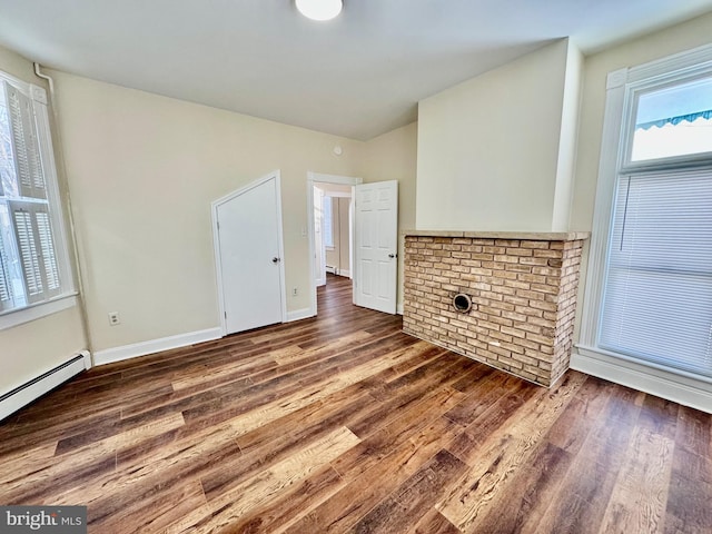 unfurnished living room featuring a baseboard heating unit and dark hardwood / wood-style floors