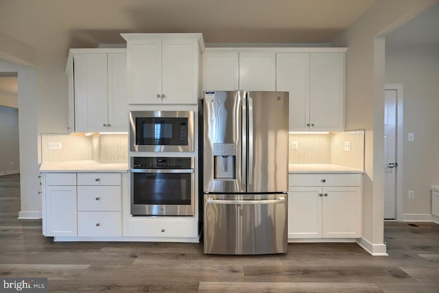 kitchen with hardwood / wood-style flooring, appliances with stainless steel finishes, backsplash, and white cabinets