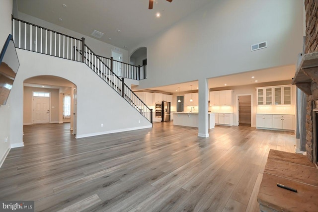 unfurnished living room with ceiling fan, a towering ceiling, sink, and hardwood / wood-style floors