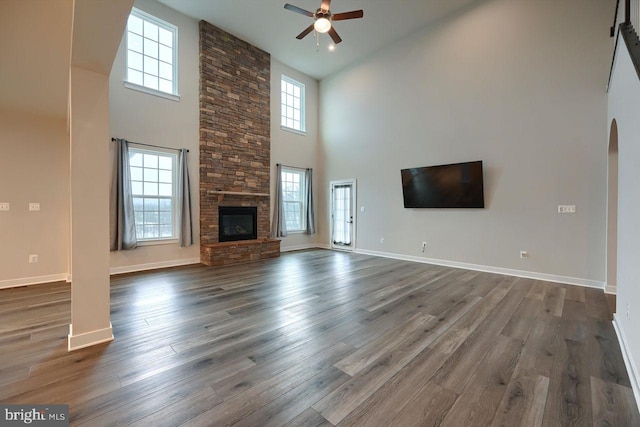 unfurnished living room featuring a fireplace, ceiling fan, dark hardwood / wood-style flooring, and a towering ceiling