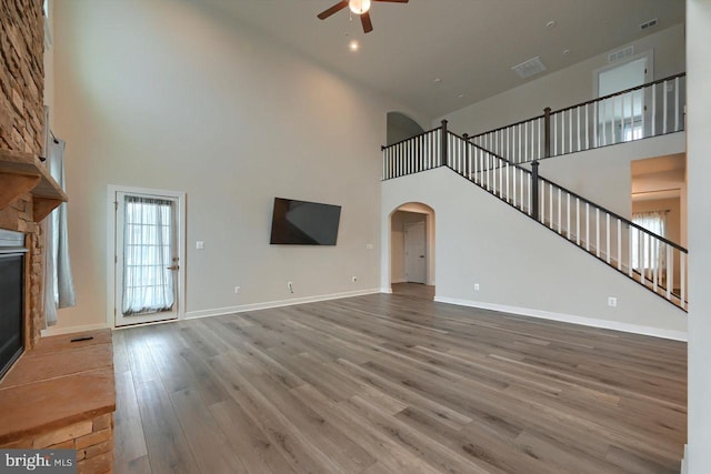 unfurnished living room with ceiling fan, a high ceiling, hardwood / wood-style floors, and a fireplace