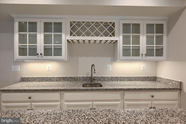 kitchen featuring sink, light stone counters, and white cabinetry