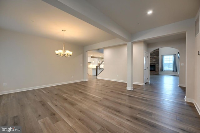 empty room featuring beam ceiling, a notable chandelier, a stone fireplace, and hardwood / wood-style floors