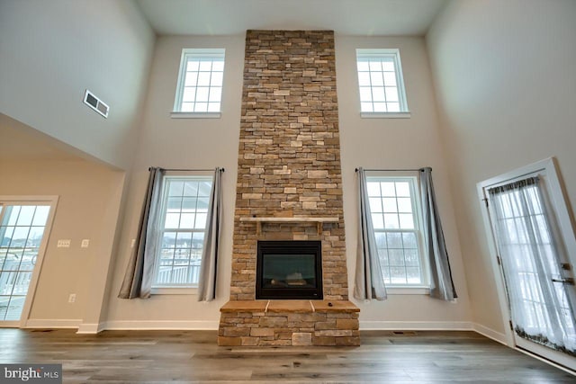 unfurnished living room with a healthy amount of sunlight, a towering ceiling, and a stone fireplace