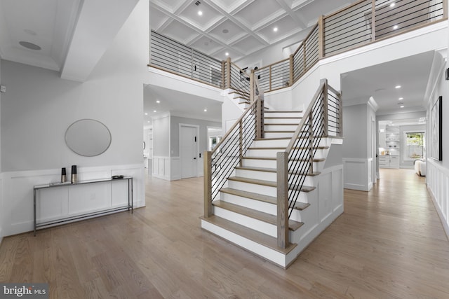 stairway with a towering ceiling, hardwood / wood-style floors, beamed ceiling, ornamental molding, and coffered ceiling