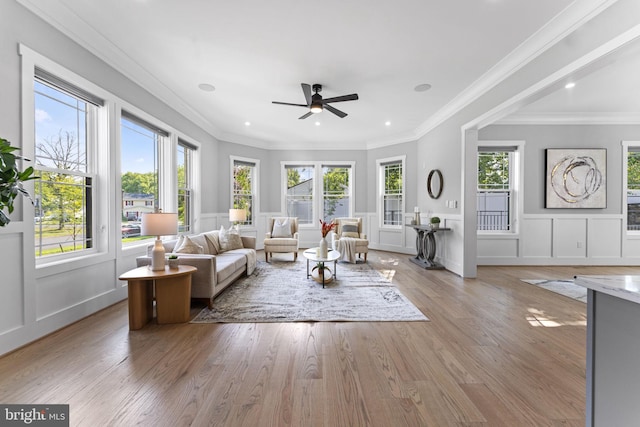 living room featuring a wealth of natural light, ornamental molding, ceiling fan, and light wood-type flooring