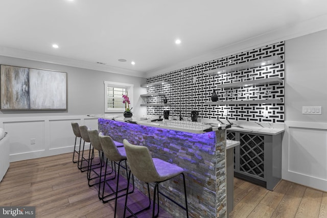 bar with light stone counters, crown molding, dark hardwood / wood-style floors, and white cabinets