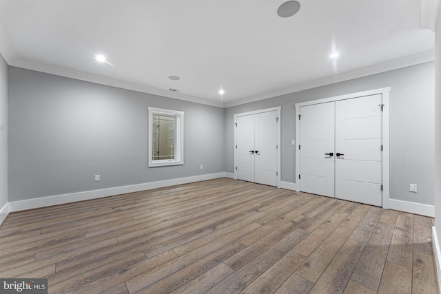 unfurnished bedroom featuring multiple closets, crown molding, and hardwood / wood-style flooring