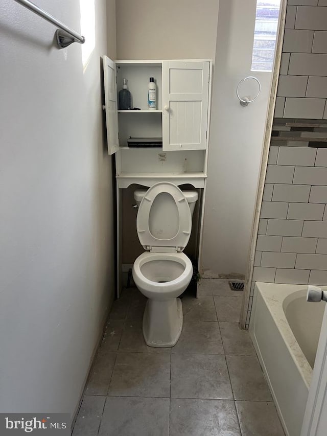 bathroom featuring toilet, tile patterned floors, and a bath