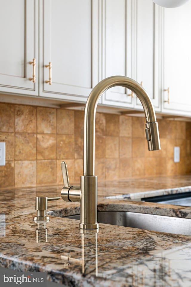 details with decorative backsplash, sink, white cabinets, and stone counters