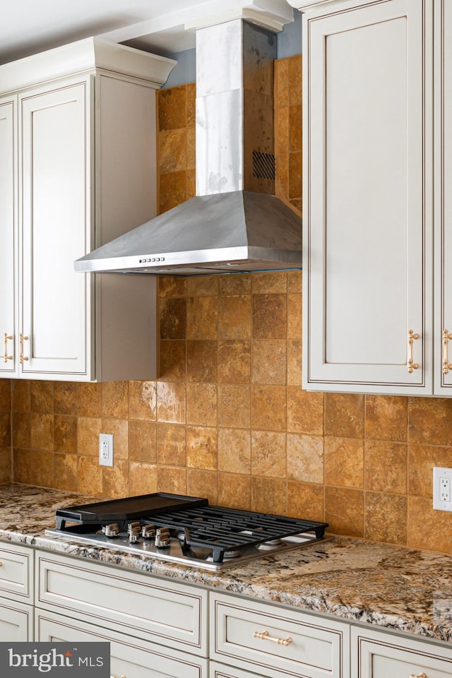 kitchen with tasteful backsplash, stainless steel gas cooktop, wall chimney range hood, white cabinets, and light stone counters