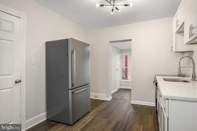 kitchen with sink, white cabinetry, dark wood-type flooring, light stone countertops, and stainless steel fridge