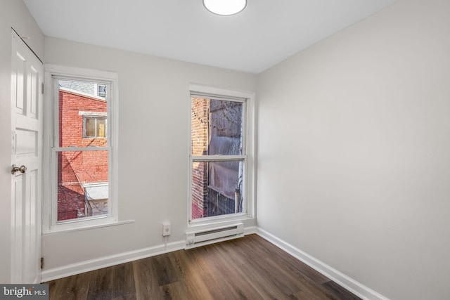 spare room featuring baseboard heating and dark wood-type flooring