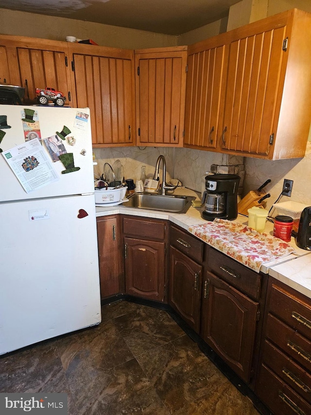 kitchen featuring white fridge, sink, dark brown cabinets, and decorative backsplash