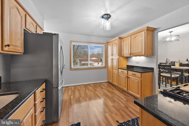 kitchen featuring pendant lighting, stainless steel refrigerator, dark stone counters, a chandelier, and light wood-type flooring