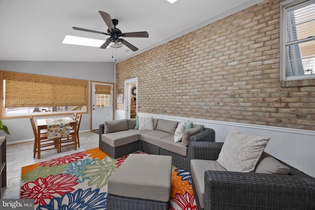 living room with ceiling fan, brick wall, and lofted ceiling with skylight