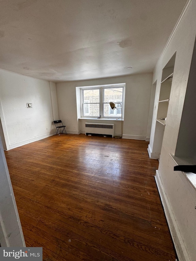 unfurnished living room with dark wood-type flooring, built in shelves, and radiator