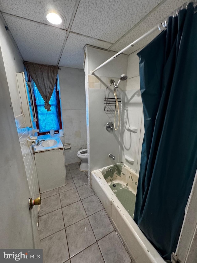 full bathroom featuring toilet, tile patterned flooring, tile walls, a drop ceiling, and shower / bath combo with shower curtain