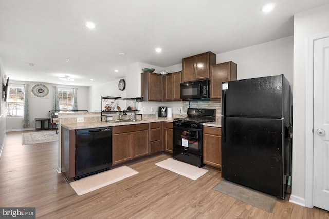 kitchen featuring light hardwood / wood-style floors, kitchen peninsula, light stone countertops, black appliances, and sink