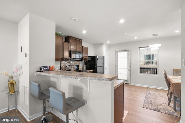 kitchen with light wood-type flooring, kitchen peninsula, hanging light fixtures, and black appliances