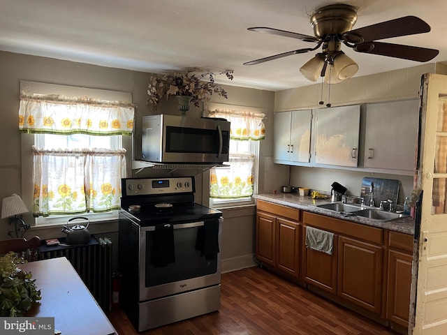 kitchen with radiator, dark wood-style floors, appliances with stainless steel finishes, brown cabinets, and a sink