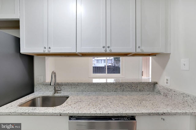 kitchen with light stone countertops, white cabinetry, stainless steel dishwasher, and sink