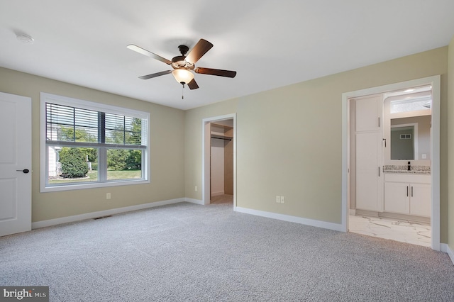 unfurnished bedroom featuring ceiling fan, a walk in closet, light colored carpet, and connected bathroom