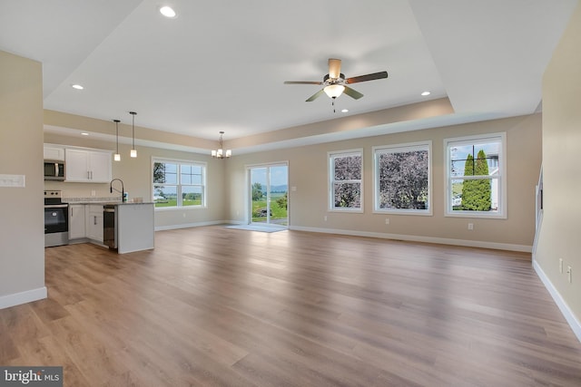 unfurnished living room featuring ceiling fan with notable chandelier, sink, and light wood-type flooring