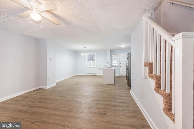 unfurnished living room featuring a textured ceiling, a baseboard radiator, sink, dark hardwood / wood-style flooring, and ceiling fan with notable chandelier