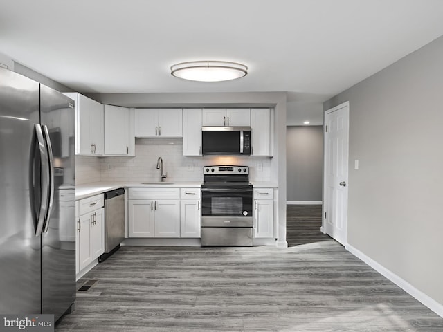 kitchen featuring backsplash, hardwood / wood-style floors, sink, stainless steel appliances, and white cabinets