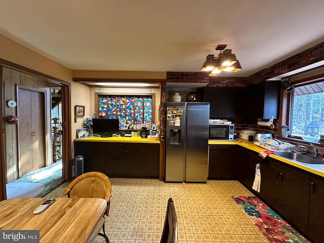 kitchen with dark brown cabinetry, stainless steel fridge, sink, and a notable chandelier