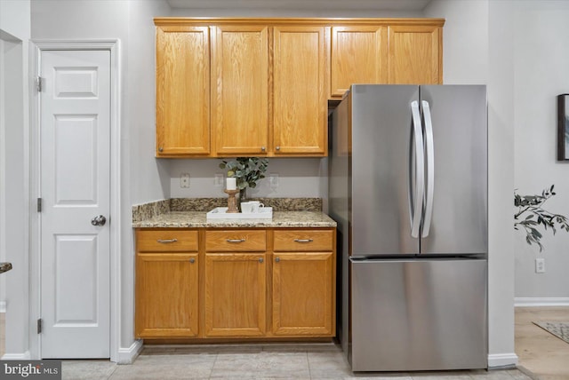 kitchen featuring light tile patterned floors, stainless steel fridge, and light stone counters